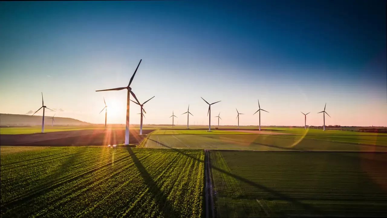 Luftaufnahme eines Windparks mit mehreren Windkraftanlagen auf einem grünen Feld im Sonnenuntergang für erneuerbare Energie und nachhaltige Entwicklung.